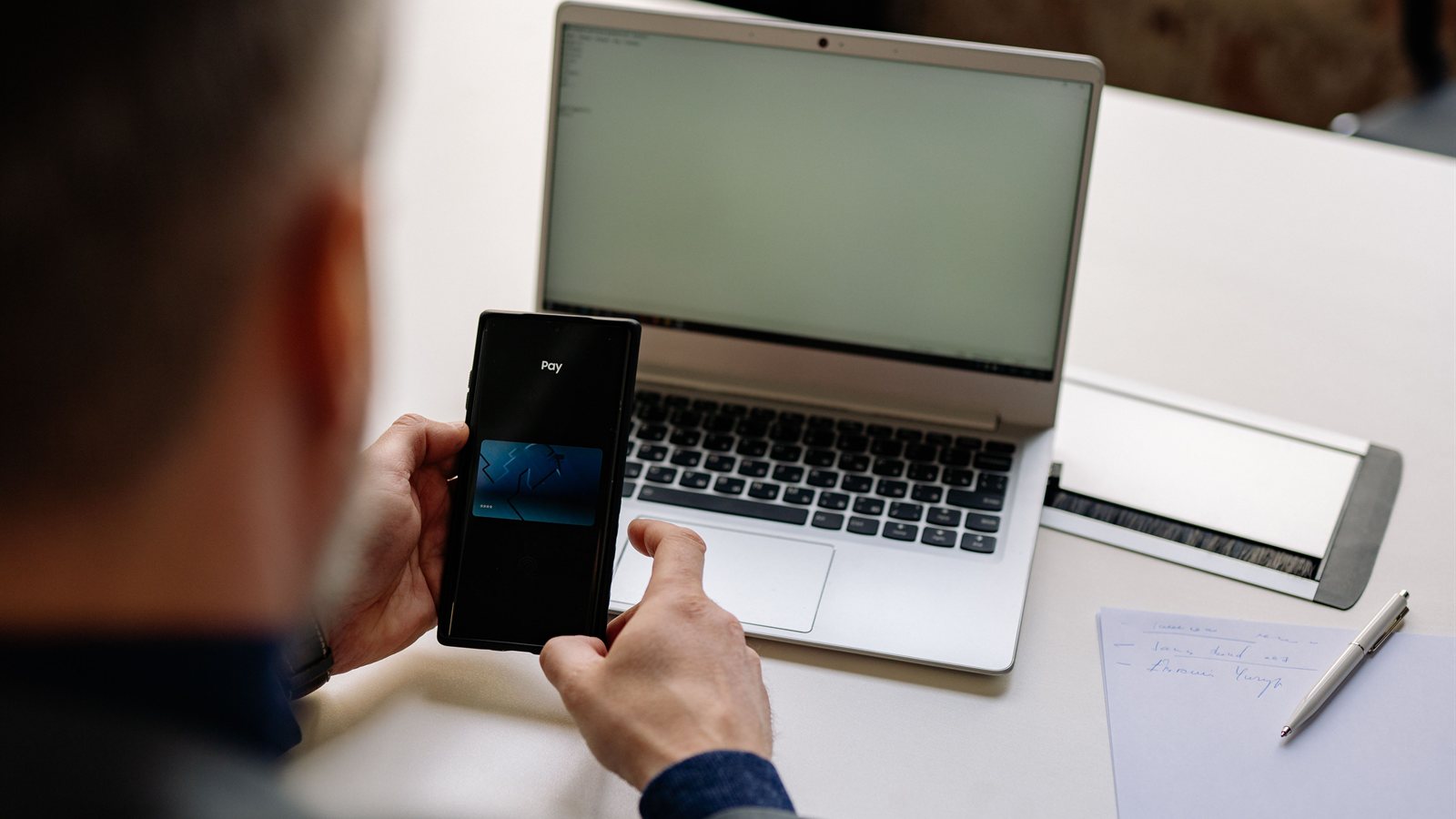 Persona realizando una transferencia desde el celular junto a un notebook